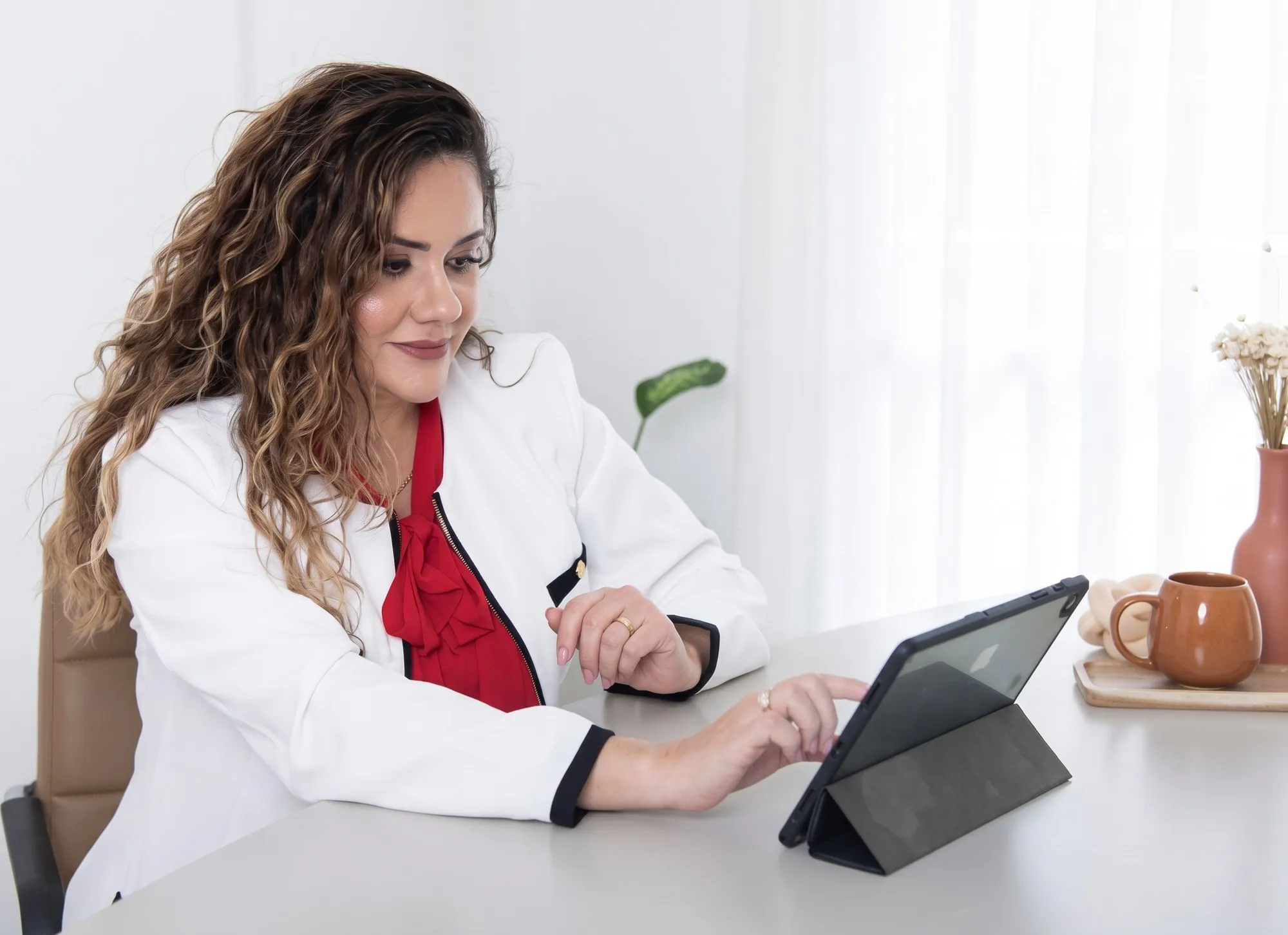 Dra. Gigliola sorrindo, sentada à mesa com um tablet